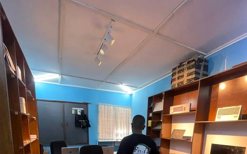 Inside the Fix-iT shop: wooden shelving holding monitors, keyboards and receipt printers, blue walls and track lighting.